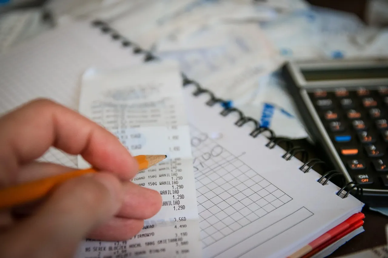 Personne vérifiant plusieurs tickets de caisse et factures à l'aide d'une calculatrice et d'un carnet de comptes