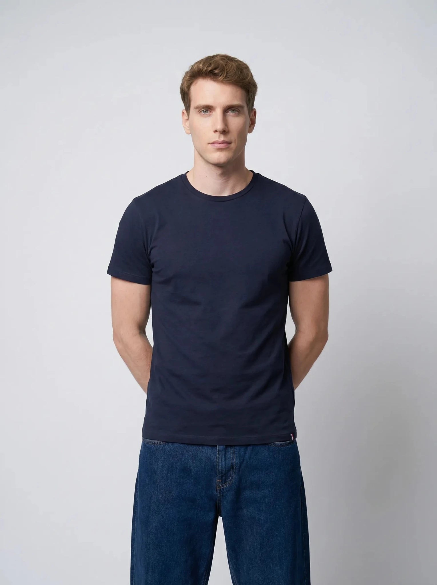 Homme portant un T-shirt bleu marine en coton, mains croisées derrière le dos